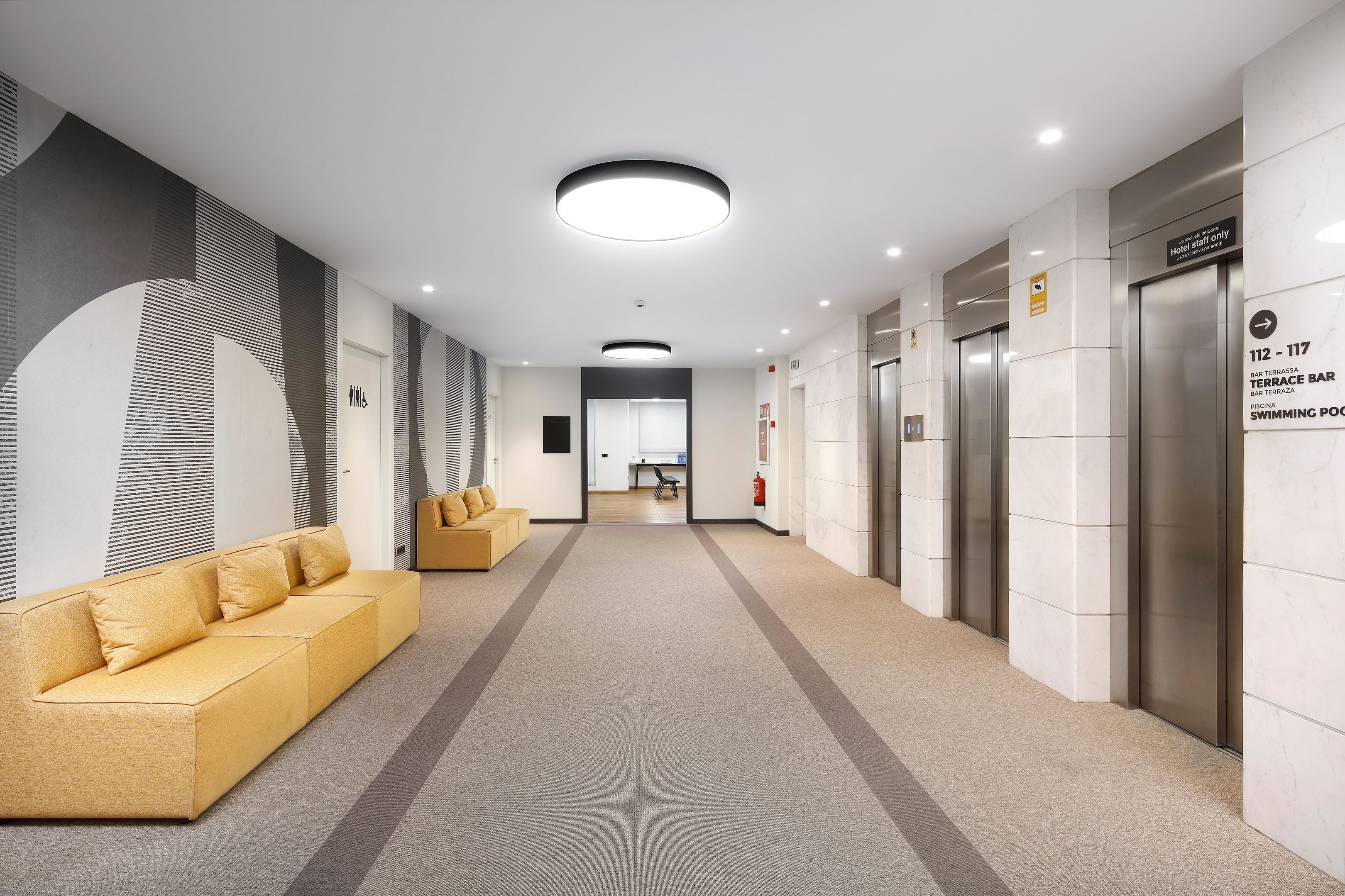 A modern hotel lobby with a long corridor, a sofa, a bar, and an elevator.