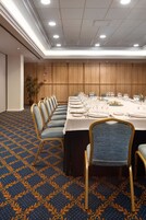 A conference room with a long table set for a meeting, blue patterned carpet, and wooden panel walls.