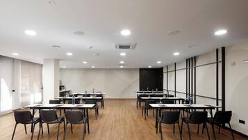 Sala de conferências com mesas e cadeiras, equipada com garrafas de água e uma grande janela lateral.