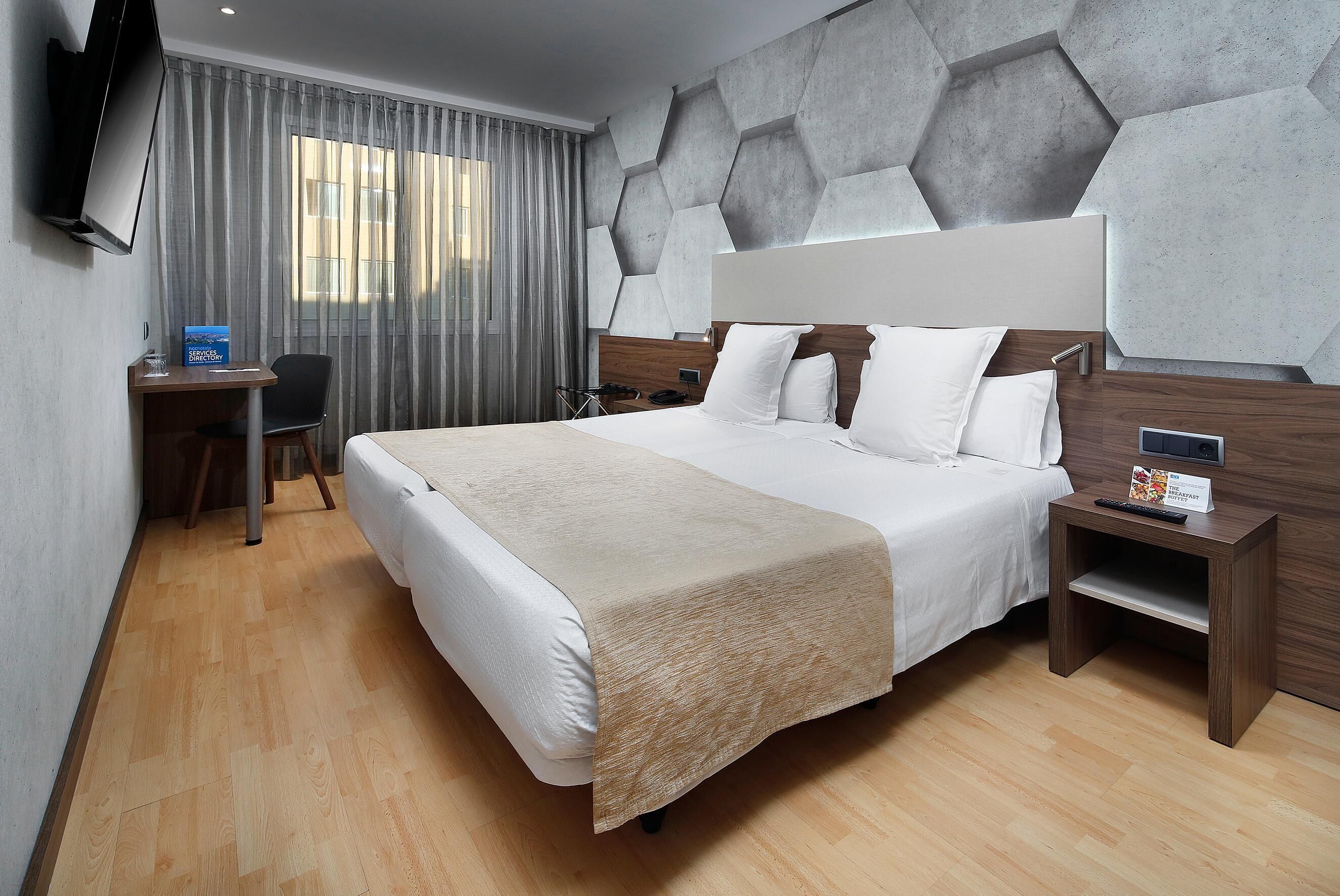 A modern hotel room with a large bed, a desk, and a TV mounted on the wall.