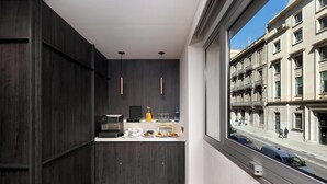 Cocina moderna con armarios de madera oscura, una cafetera y vistas a una calle de la ciudad a través de un ventanal grande.