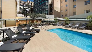 A rooftop pool area with sun loungers and umbrellas, surrounded by buildings. - Hotel HCC MontBlanc (Barcelona)
