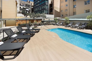 A rooftop pool area with sun loungers and umbrellas, surrounded by buildings. - Hotel HCC MontBlanc (Barcelona)