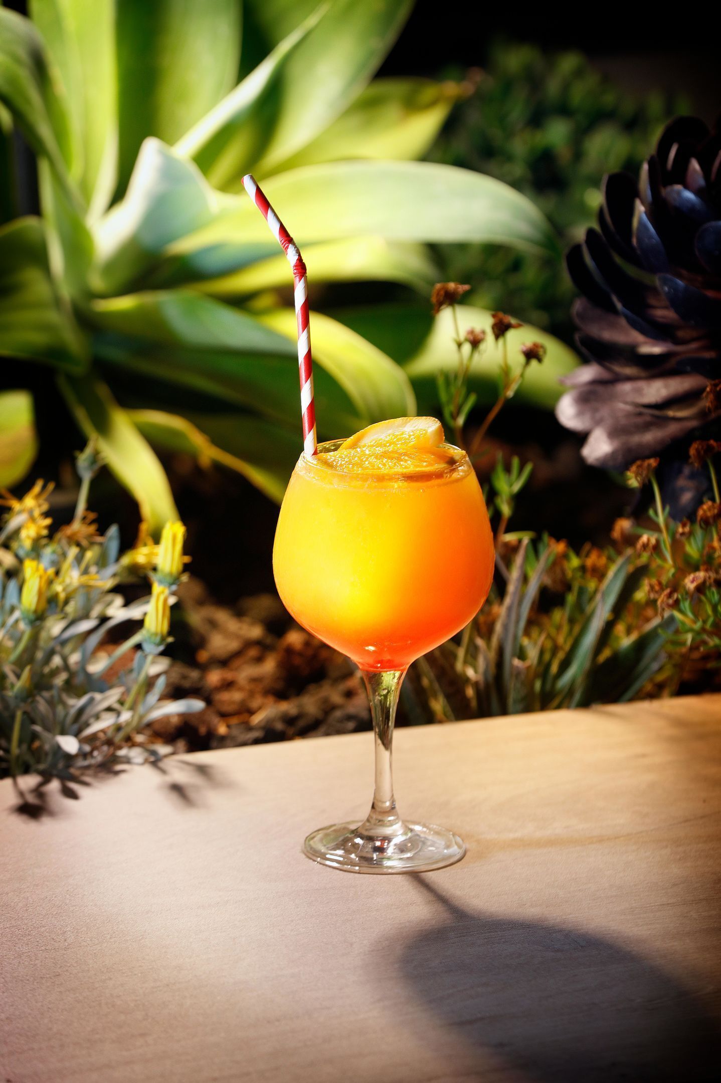 A cocktail glass with a striped straw on a wooden table.