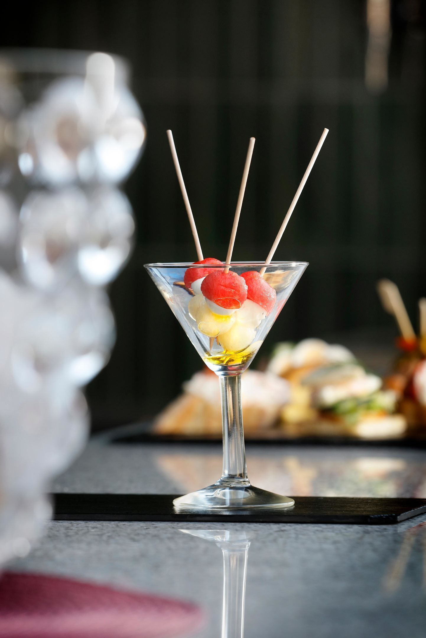A martini glass with a cocktail garnish on a reflective surface.