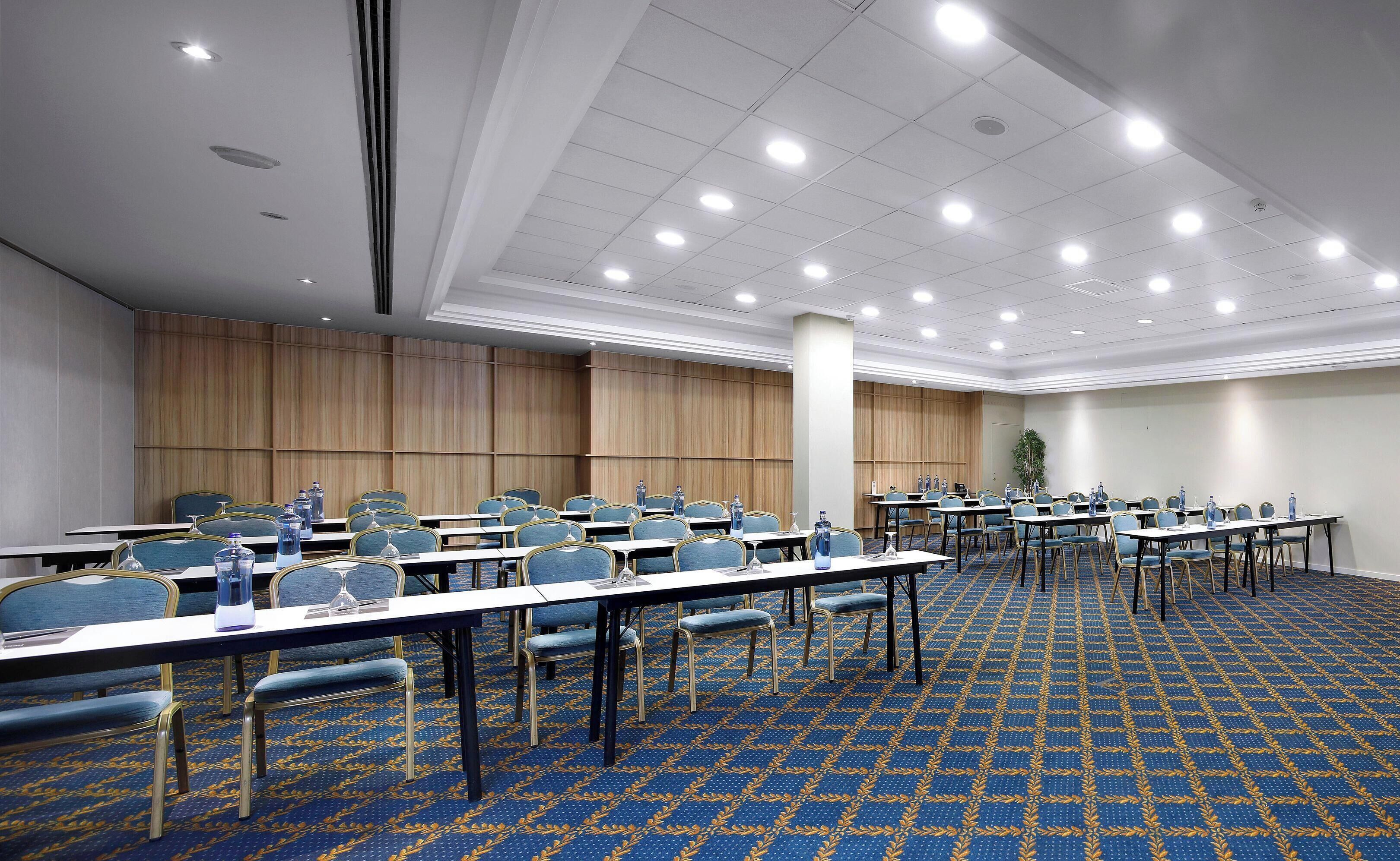 A conference room with multiple tables and chairs, a patterned carpet, and a wooden panel wall.