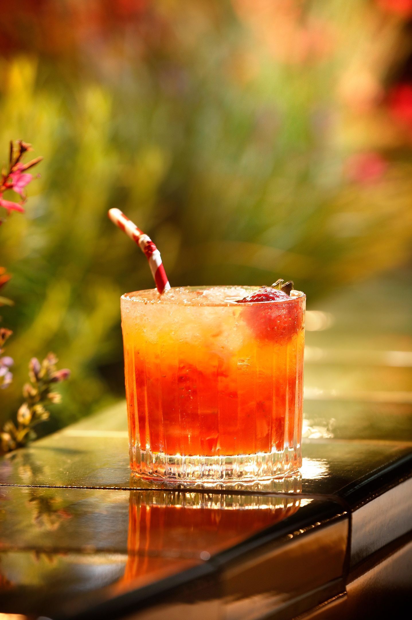 A glass of iced beverage with a straw on a reflective surface.