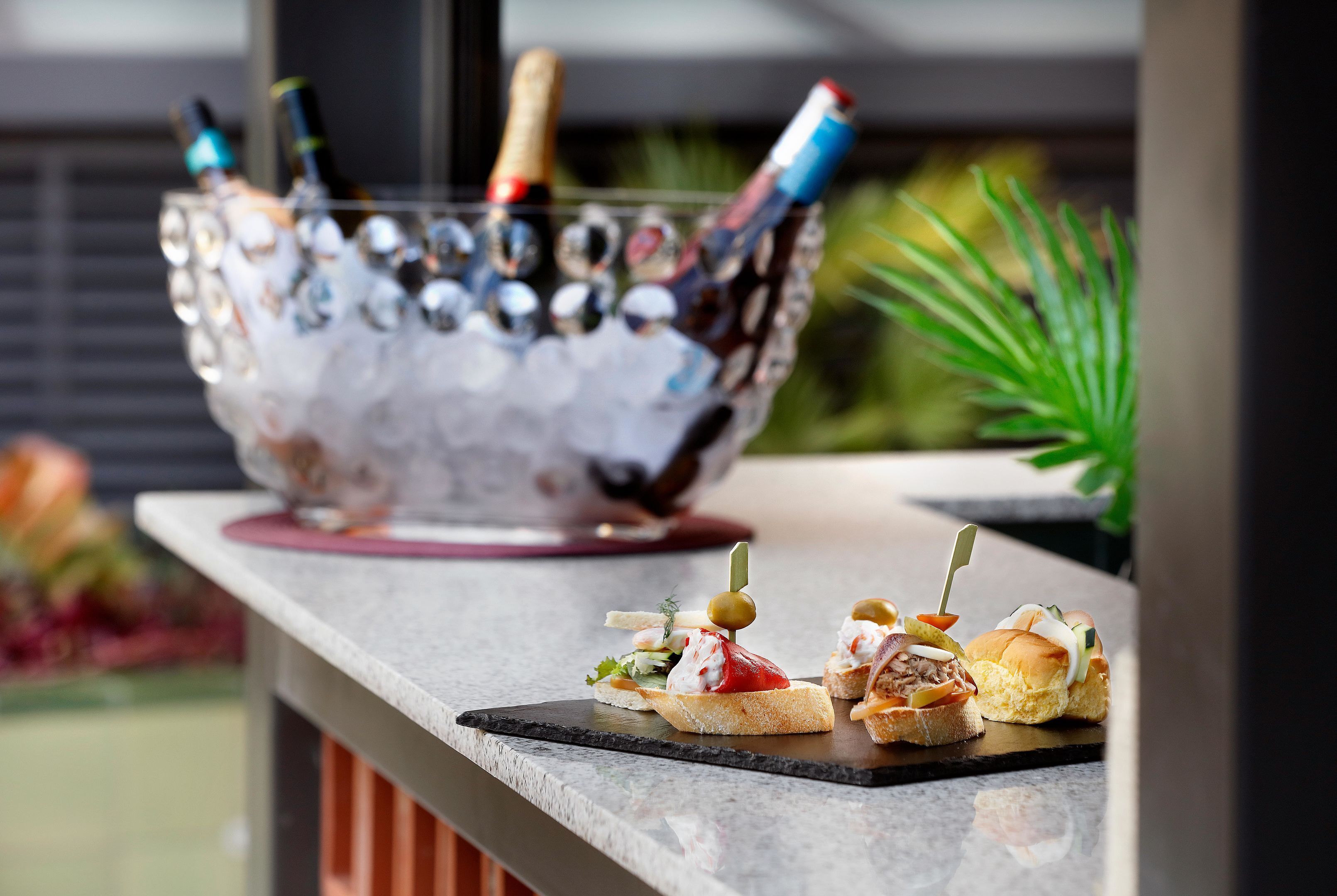 Eine Bar mit einer Glasbowl, gefüllt mit Flaschen und einer Champagnerflasche. Auf einer Marmorplatte liegen zwei kleine Teller mit Vorspeisen.