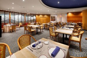 Um restaurante com mesas redondas, cadeiras de madeira e piso coberto por carpete.