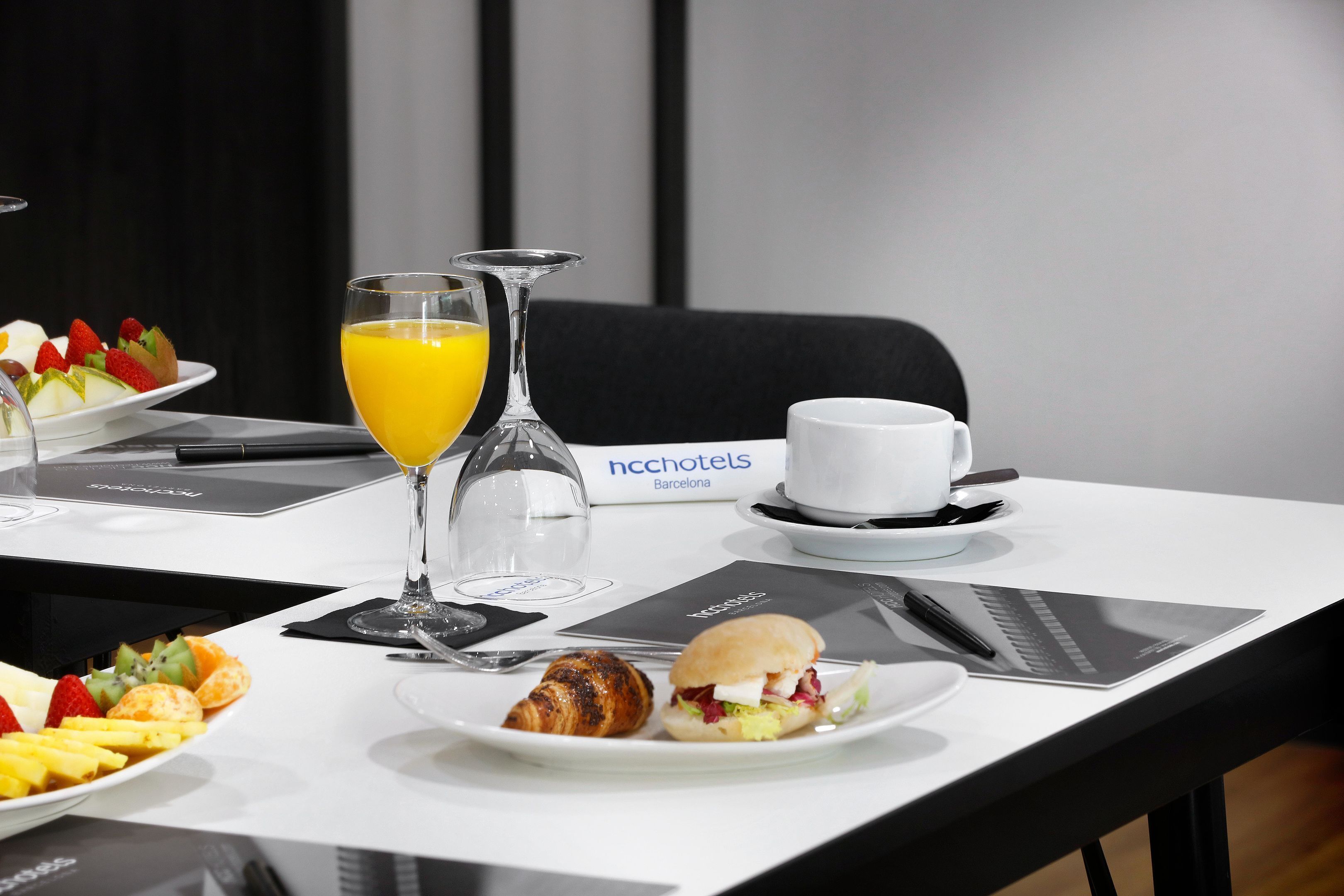 A breakfast setting with croissants, a sandwich, fruit, and orange juice on a hotel table.