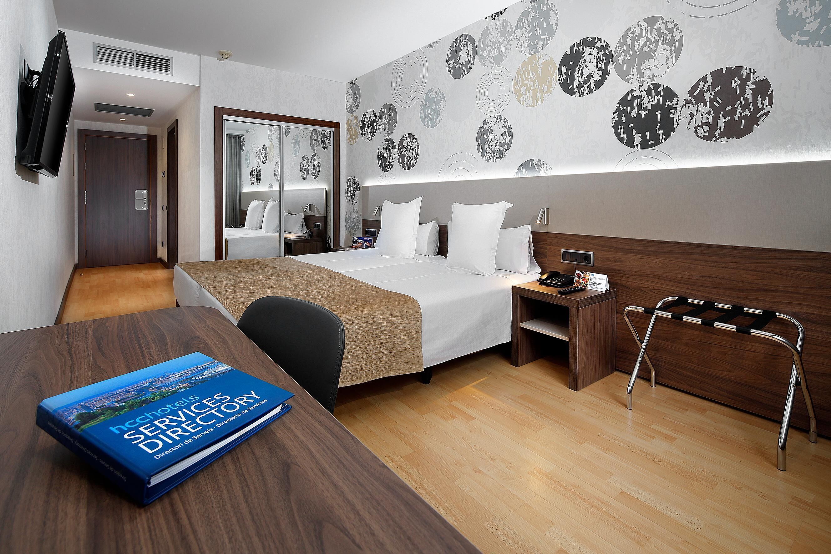Une chambre d’hôtel avec un lit, une table de chevet et un bureau sur lequel se trouve un livre.