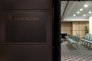 Una sala de conferencias con un cartel que dice "SALA TRAFALGAR" y filas de sillas azules con detalles dorados.