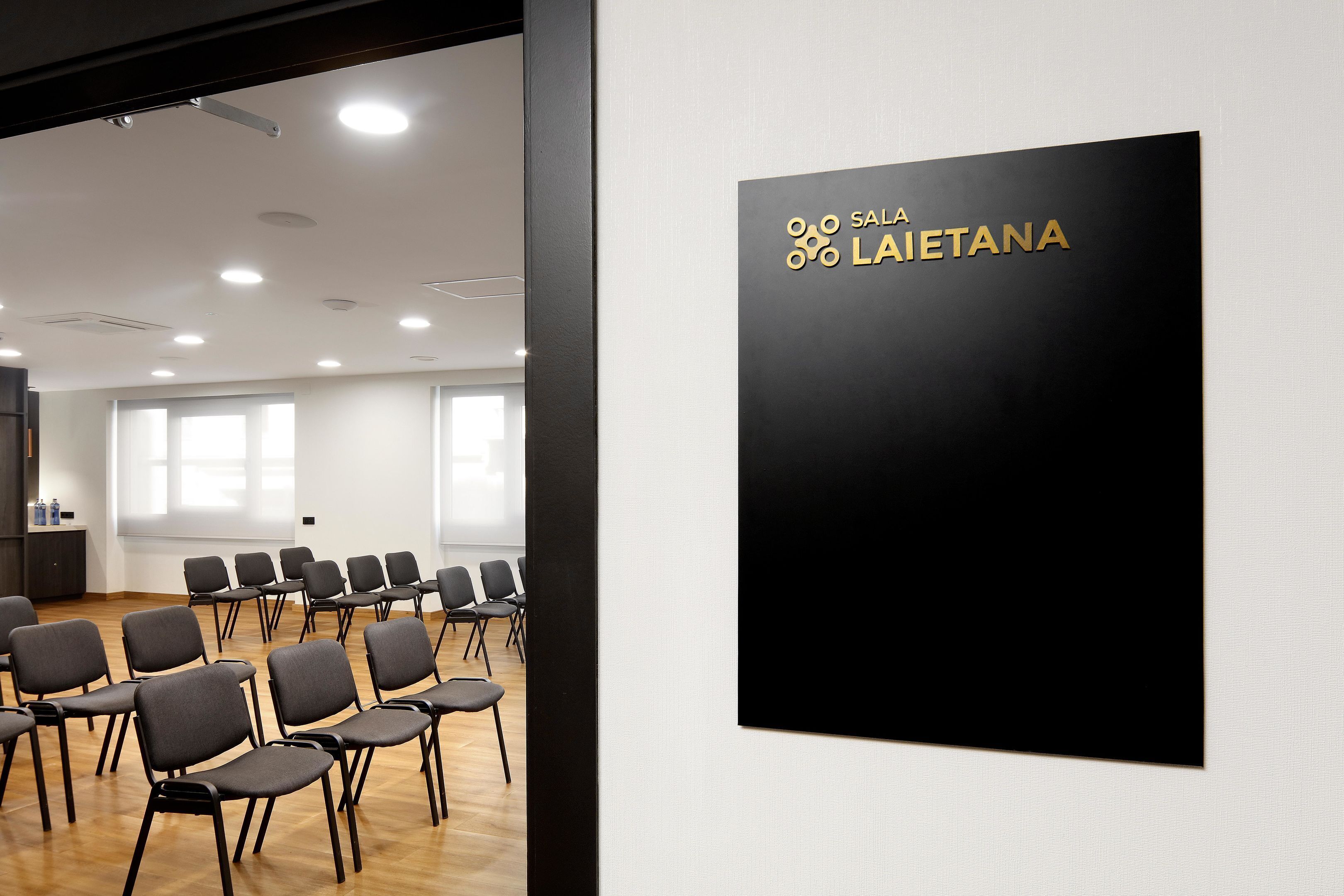 A conference room with rows of chairs and a black sign with gold text reading "SALA LAIETANA".