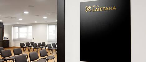 A conference room with rows of chairs and a black sign with gold text reading "SALA LAIETANA".