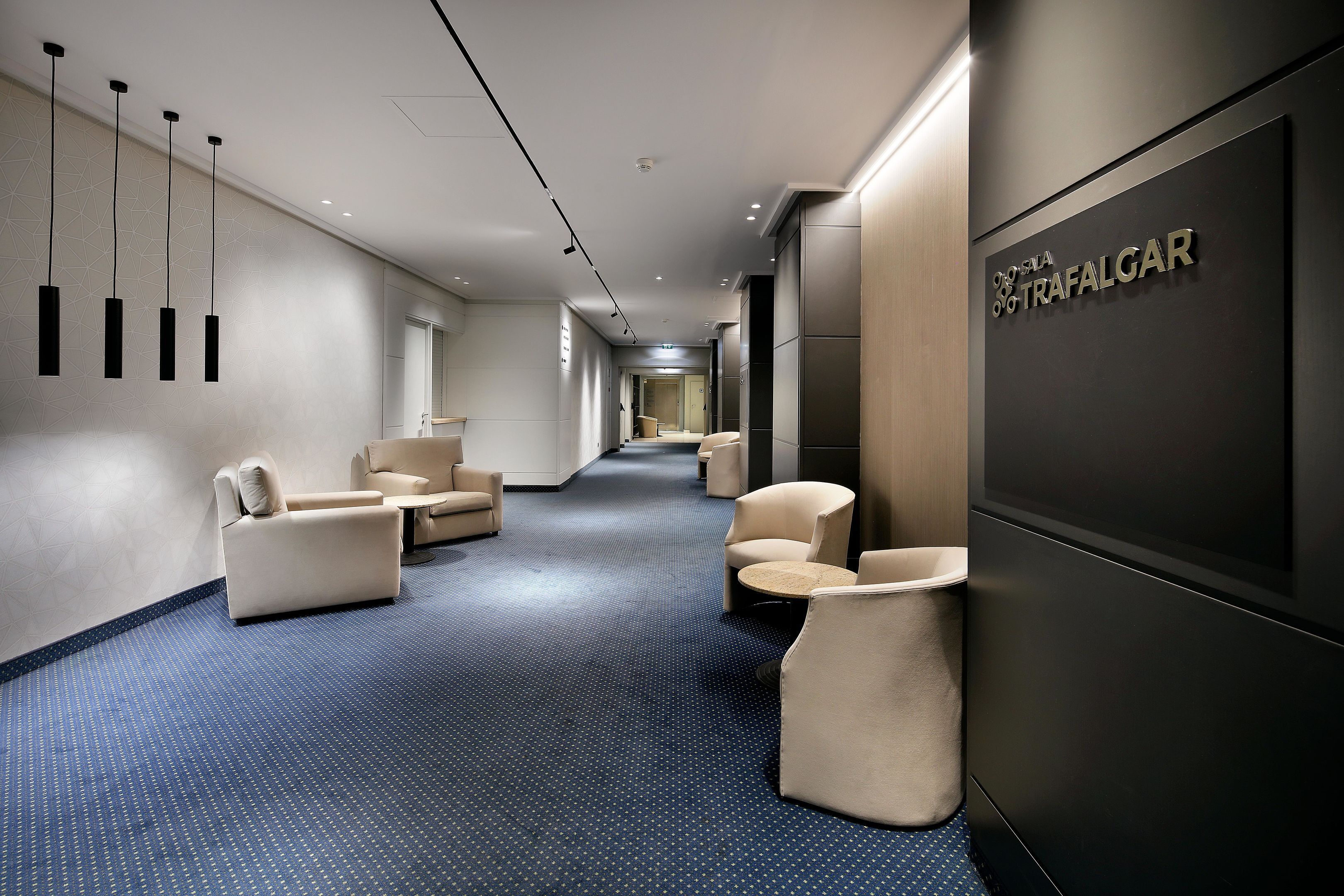 A modern hotel corridor with seating areas, a reception desk, and a sign reading "Trafalgar".