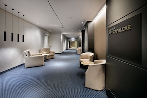 Un pasillo moderno de hotel con zonas de estar, un mostrador de recepción y un cartel que dice "Trafalgar".