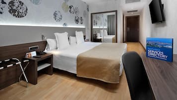 A hotel room with a large bed, bedside tables, a desk, a chair, a flat-screen TV, and a signboard.