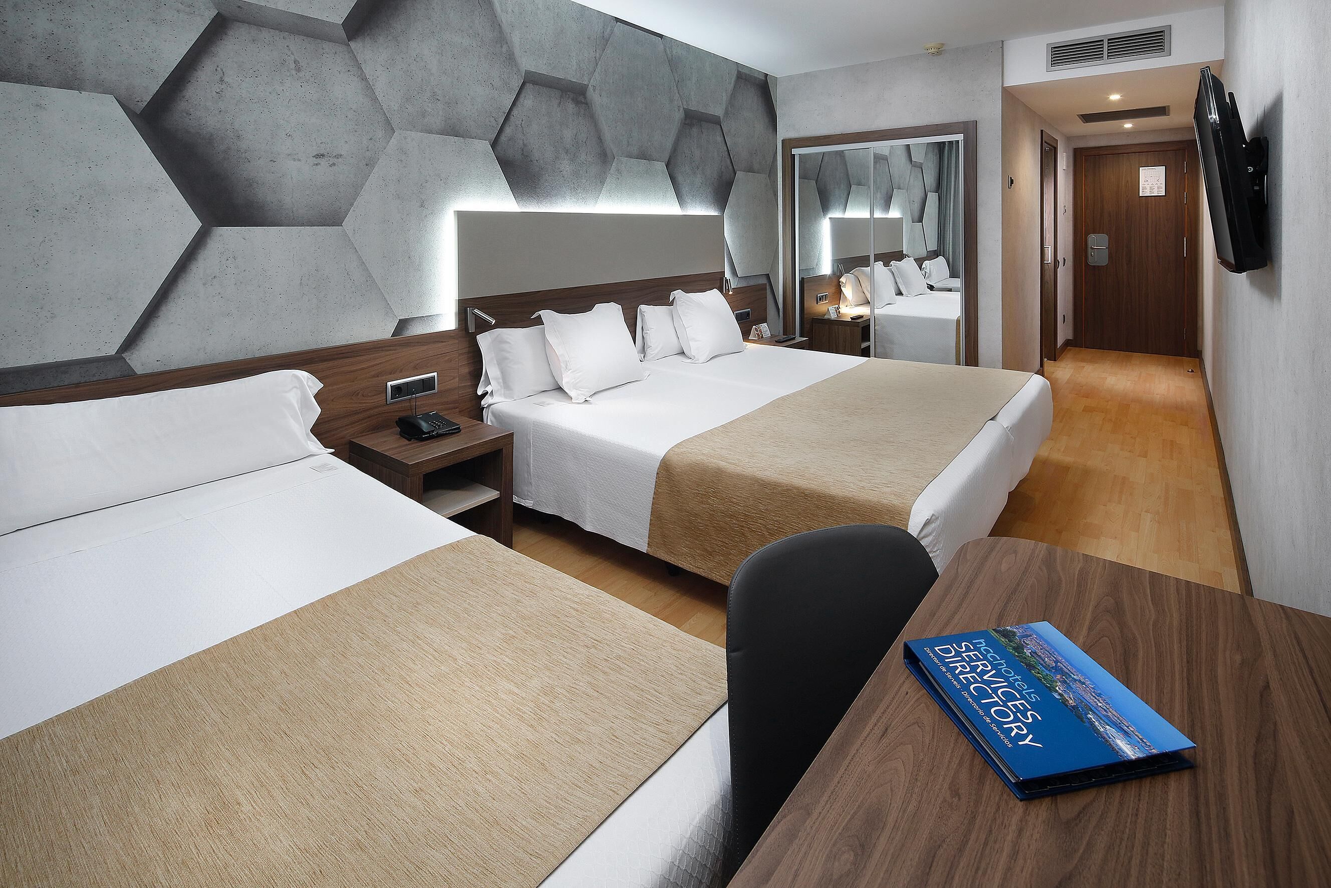 Habitació d'hotel amb dos llits, un escriptori de fusta, un llibre anomenat "Hotel Services Directory" i un mirall a la paret.