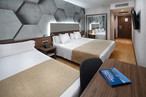 A hotel room with two beds, a wooden desk, a book titled "Hotel Services Directory," and a mirror on the wall.