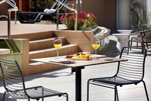 Une terrasse extérieure avec une table et des chaises, une assiette de fruits et deux verres de jus d’orange.