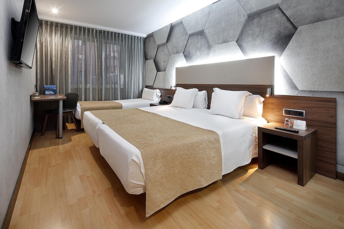 A modern hotel room with two beds, a desk, and a television.