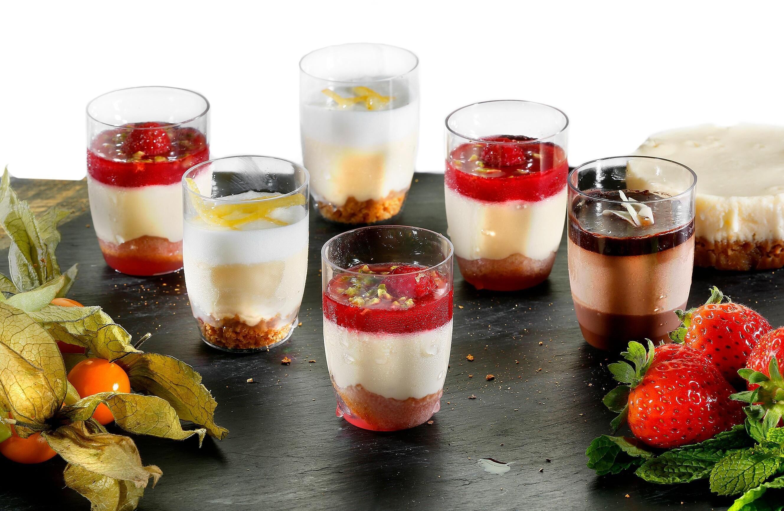 A dessert display with various layered desserts in glasses and a cheesecake on the side.