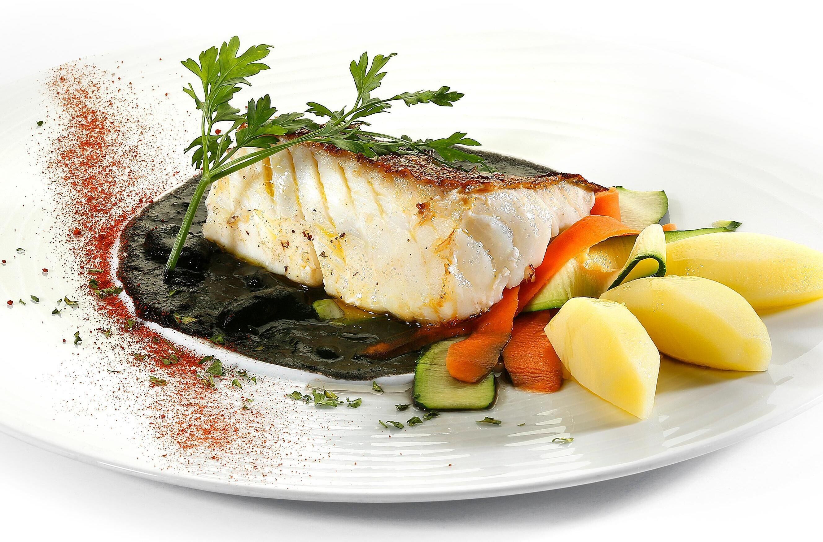A plate with a piece of fish, vegetables, and a garnish.