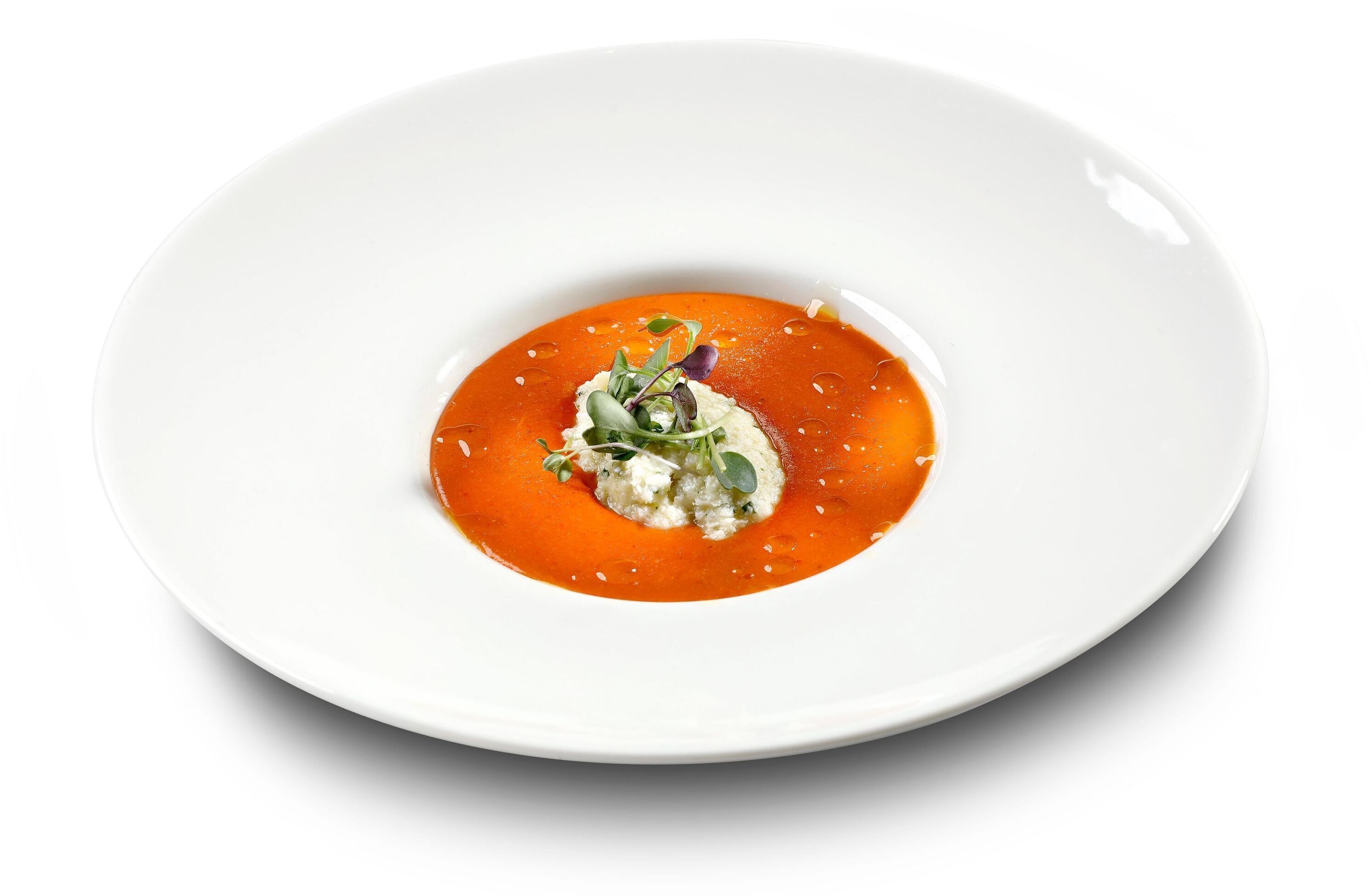 Un plato blanco con salsa roja y una cucharada de crema en el centro, decorado con vegetales y una hoja morada.