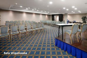 Un salón de conferencias con filas de sillas, una mesa larga y una alfombra estampada.