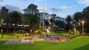 A park with playground equipment, palm trees, and a tower in the background. - Parkside Hotel & Apartments Auckland (Auckland)