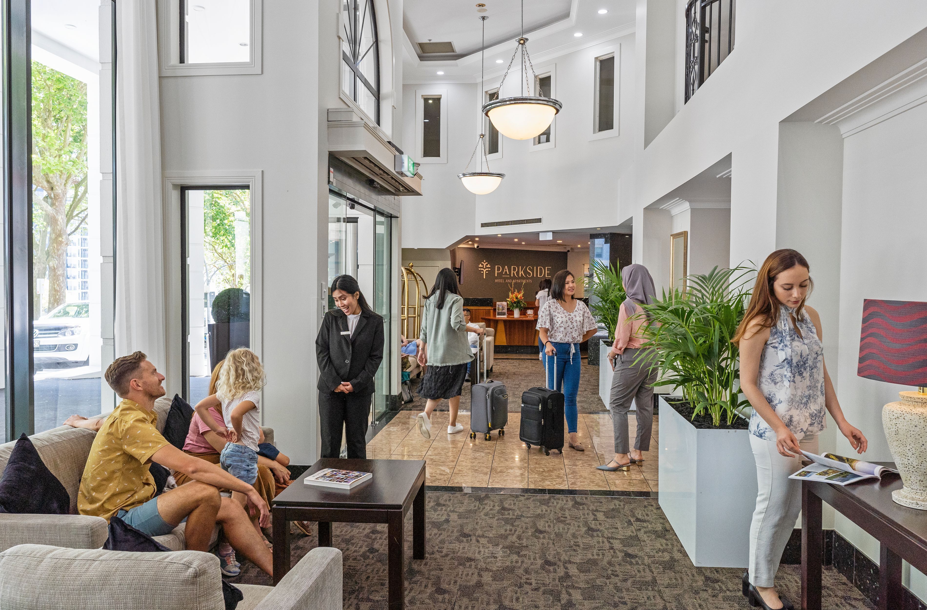 A hotel lobby with a reception desk, seating area, and a large window overlooking the street.