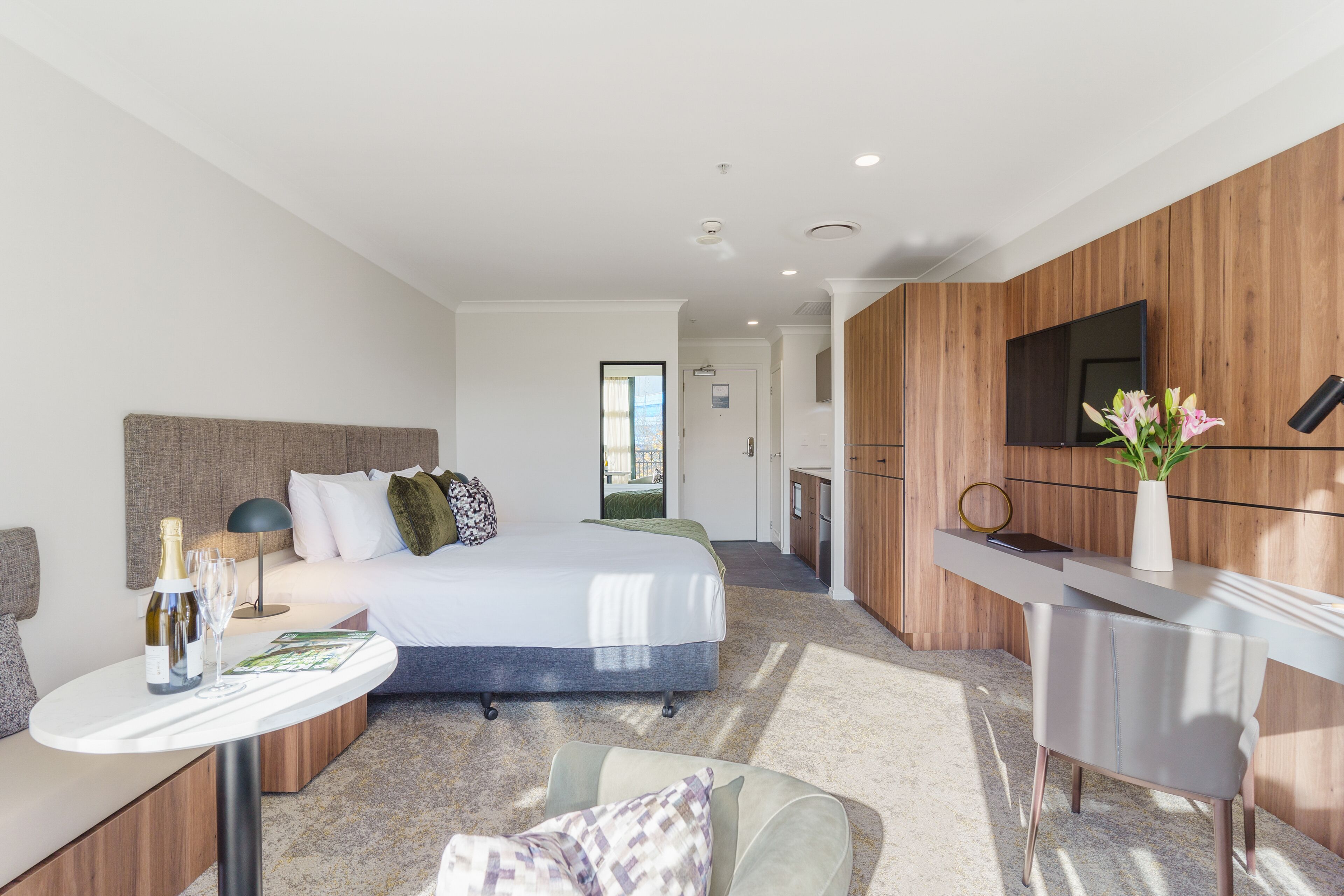 Quarto de hotel moderno com cama, mesa de cabeceira e área de trabalho.