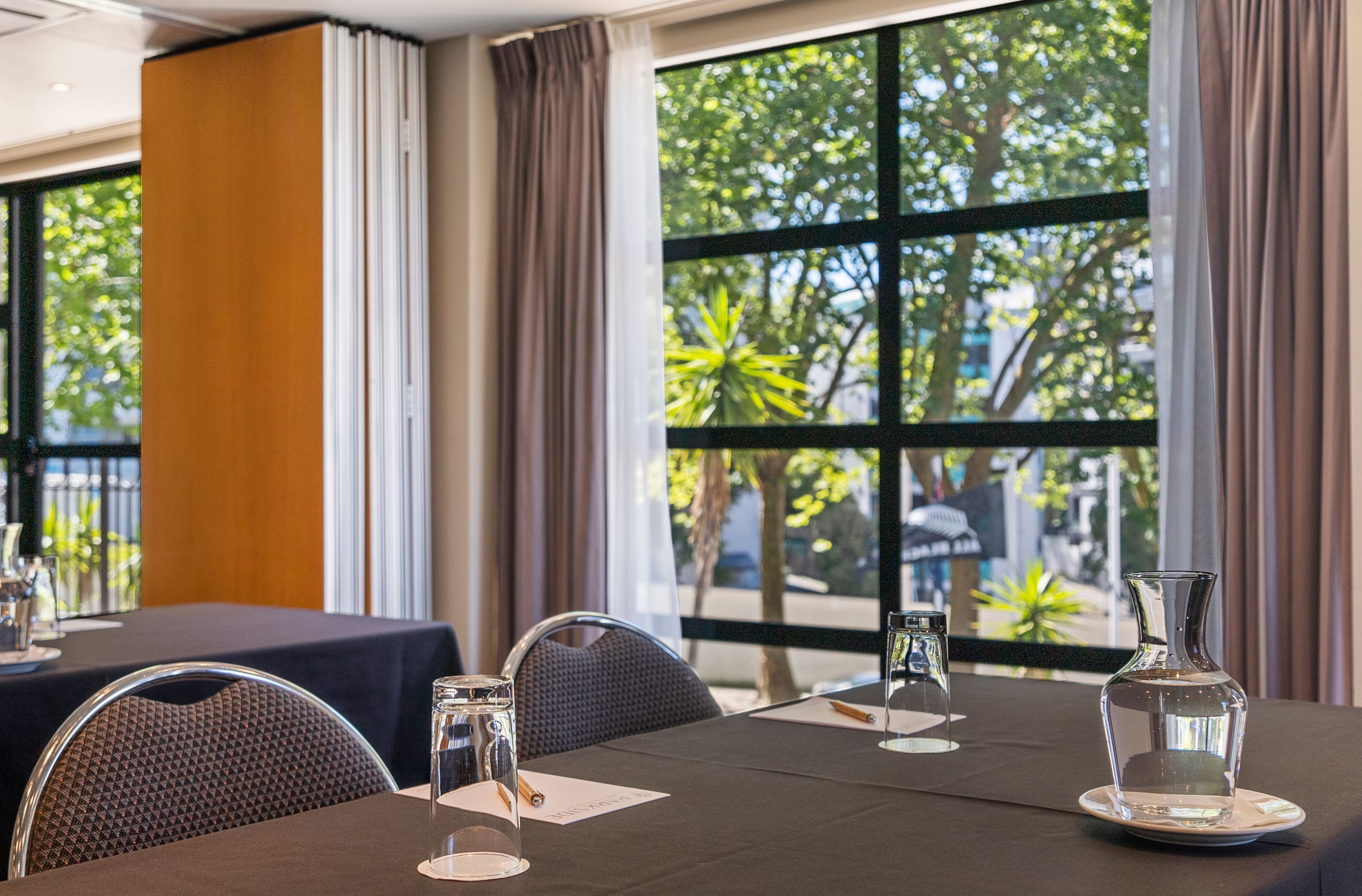 A conference room with a table set for a meeting, large windows with a view of trees and buildings, and a modern interior design.