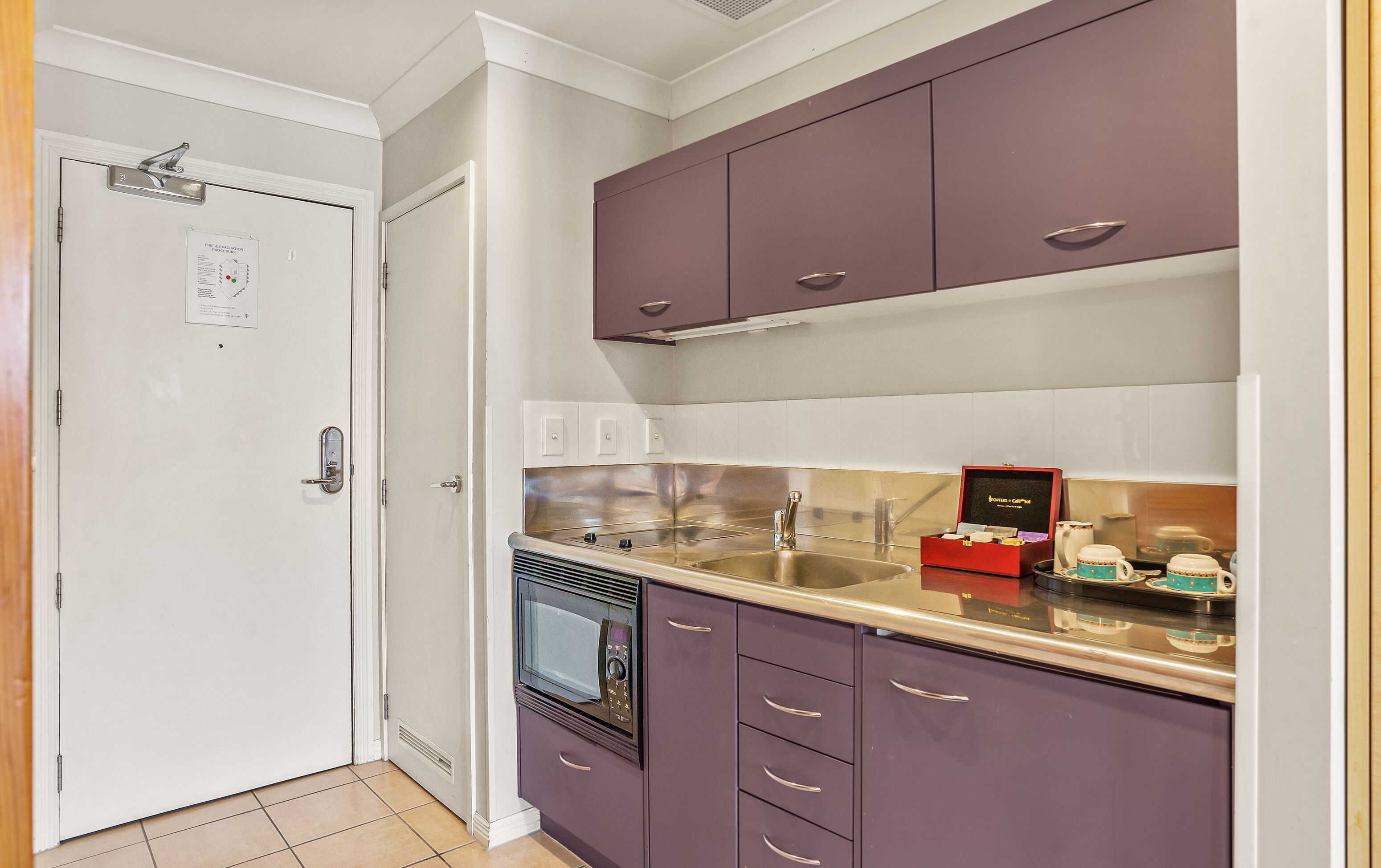 A kitchen with purple cabinets, a stainless steel sink, and a microwave.