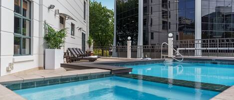 A swimming pool with lounge chairs and a modern building with large windows in the background.