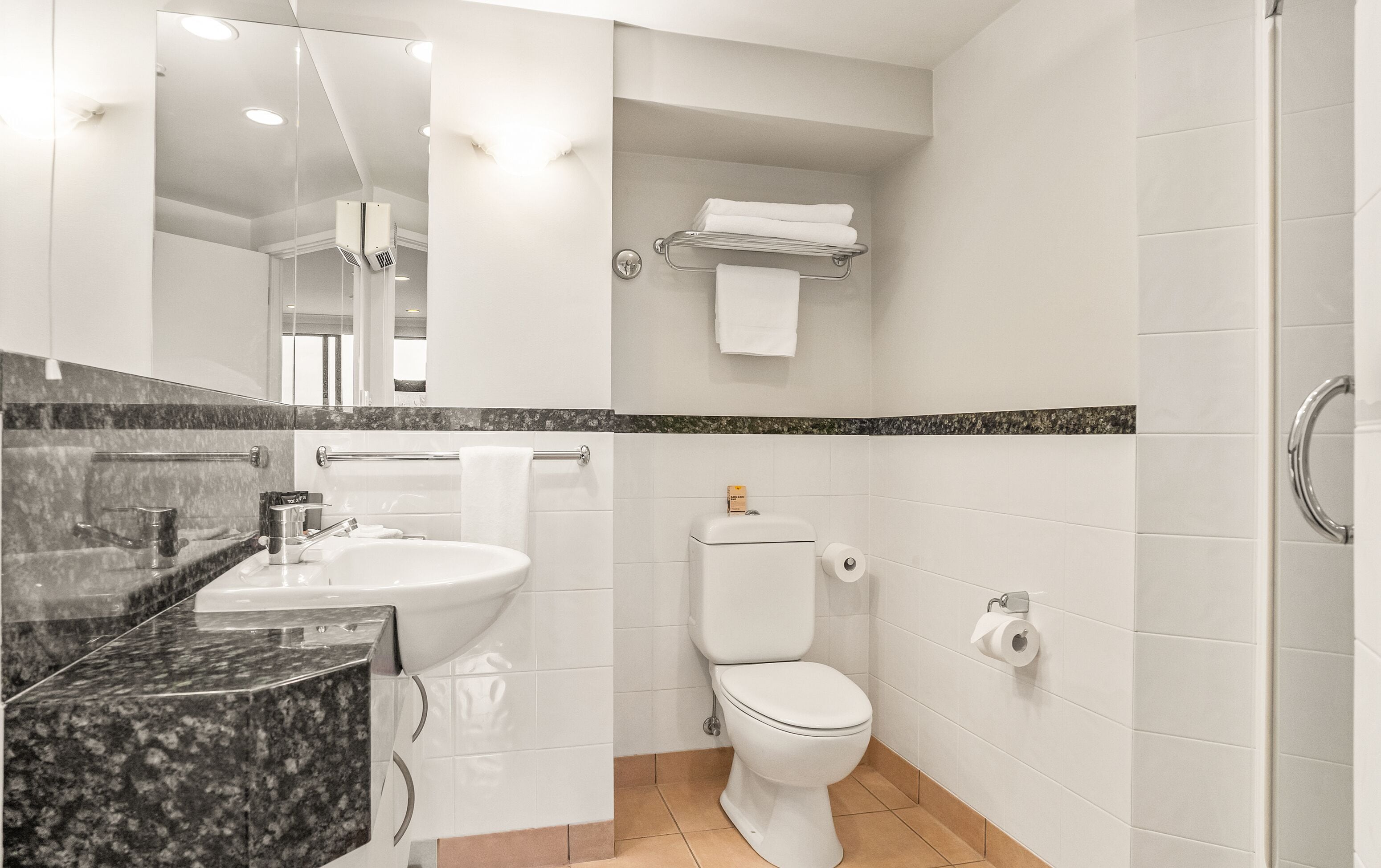 Un baño moderno con lavamanos, inodoro y perchero para toallas.