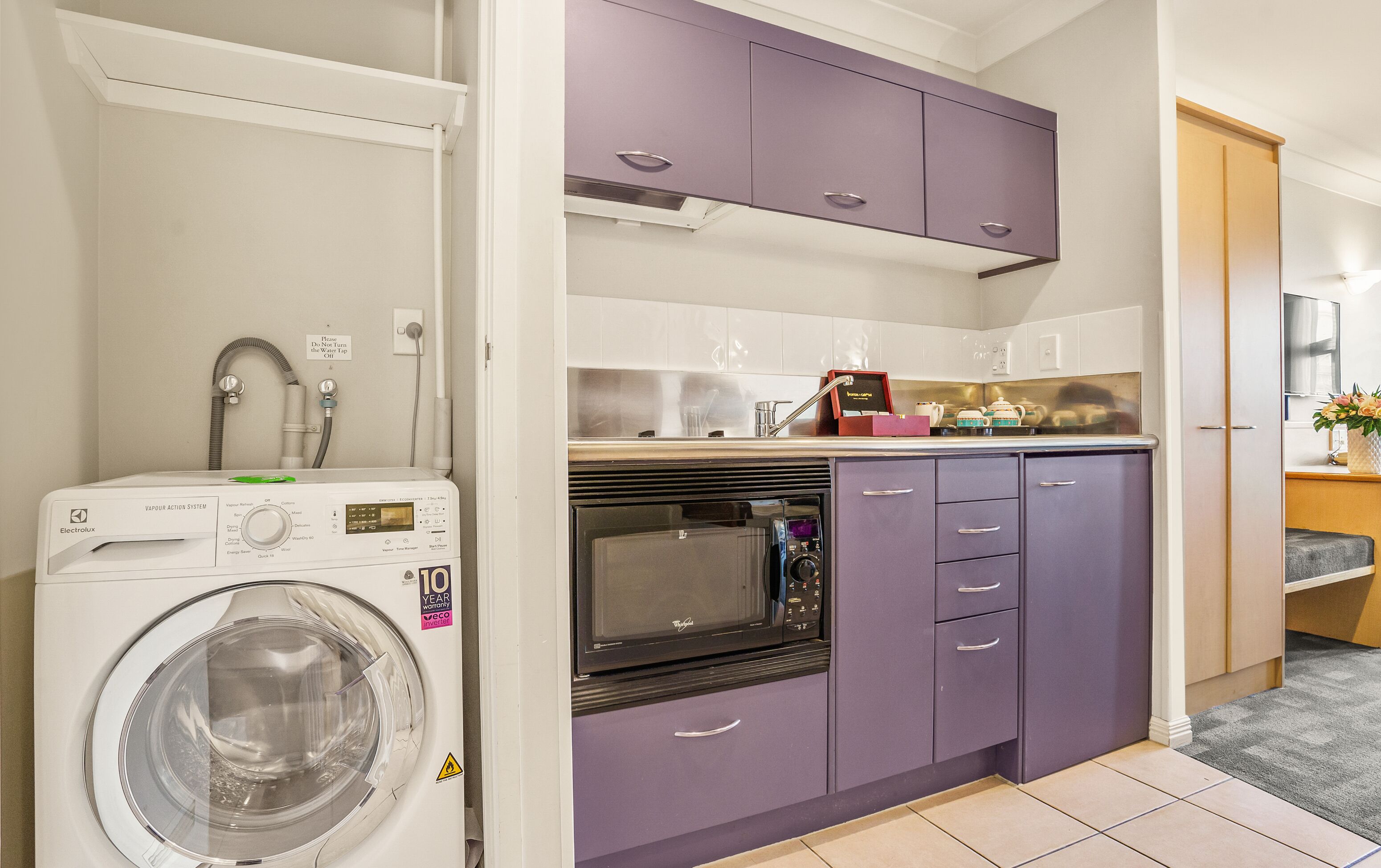 Une cuisine de taille réduite équipée d’un lave-linge, d’un four à micro-ondes et de meubles de couleur violette.