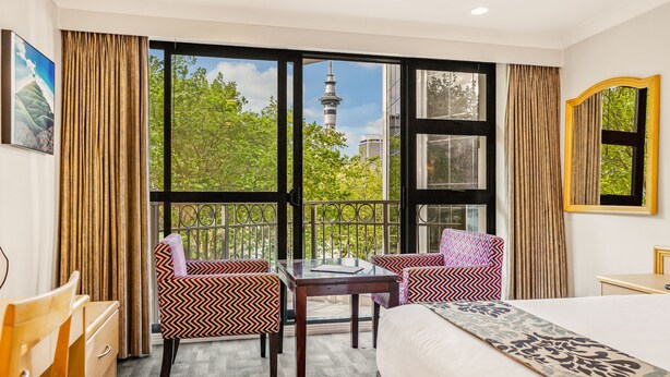 A hotel room with a large window, a bed, a desk, and two patterned chairs. - Parkside Hotel & Apartments Auckland (Auckland)
