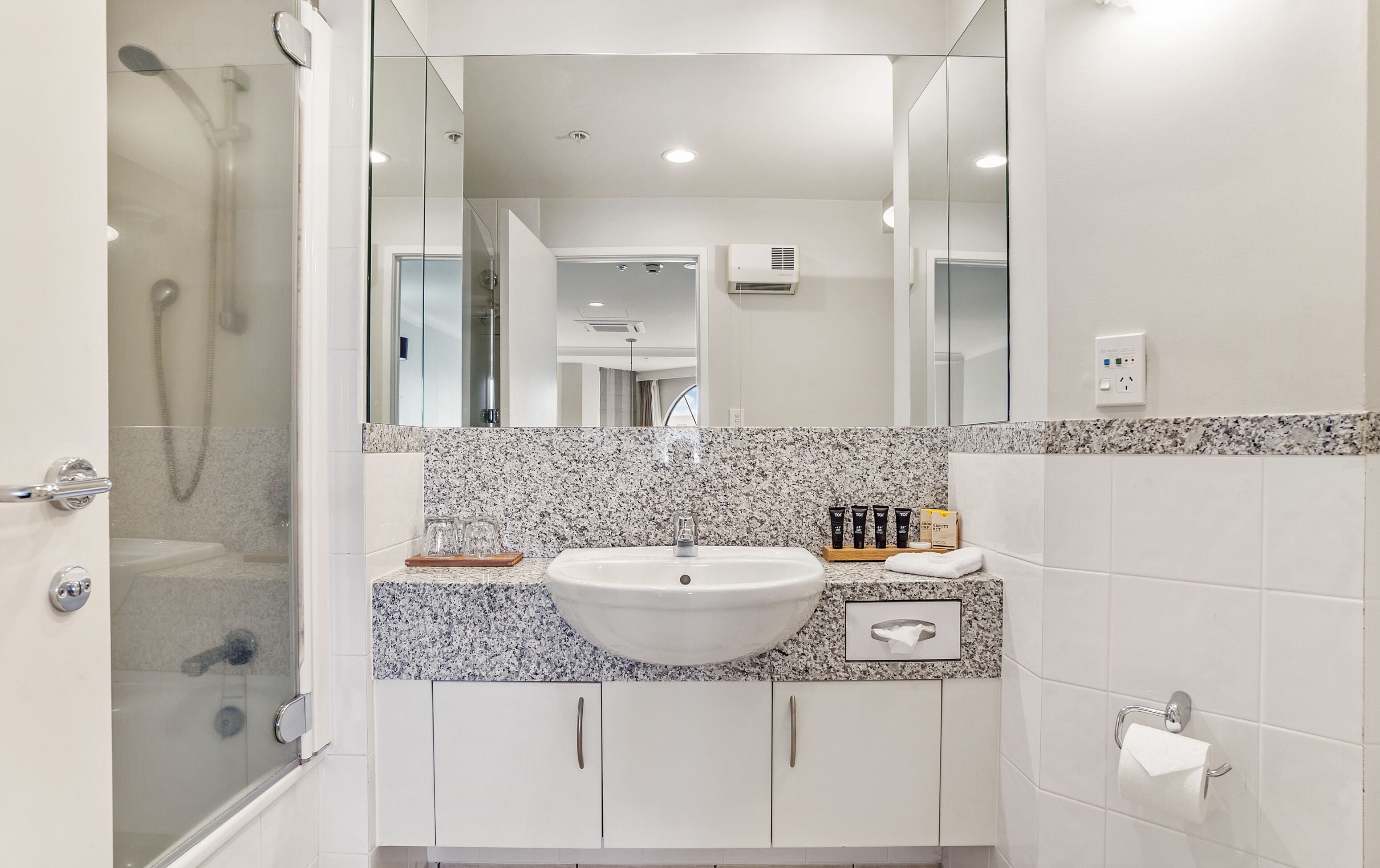 Une salle de bain avec un lavabo blanc, un comptoir en granit et une cabine de douche en verre.