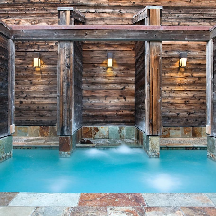 A wooden interior with a pool, stone walls, and two wall-mounted lights.