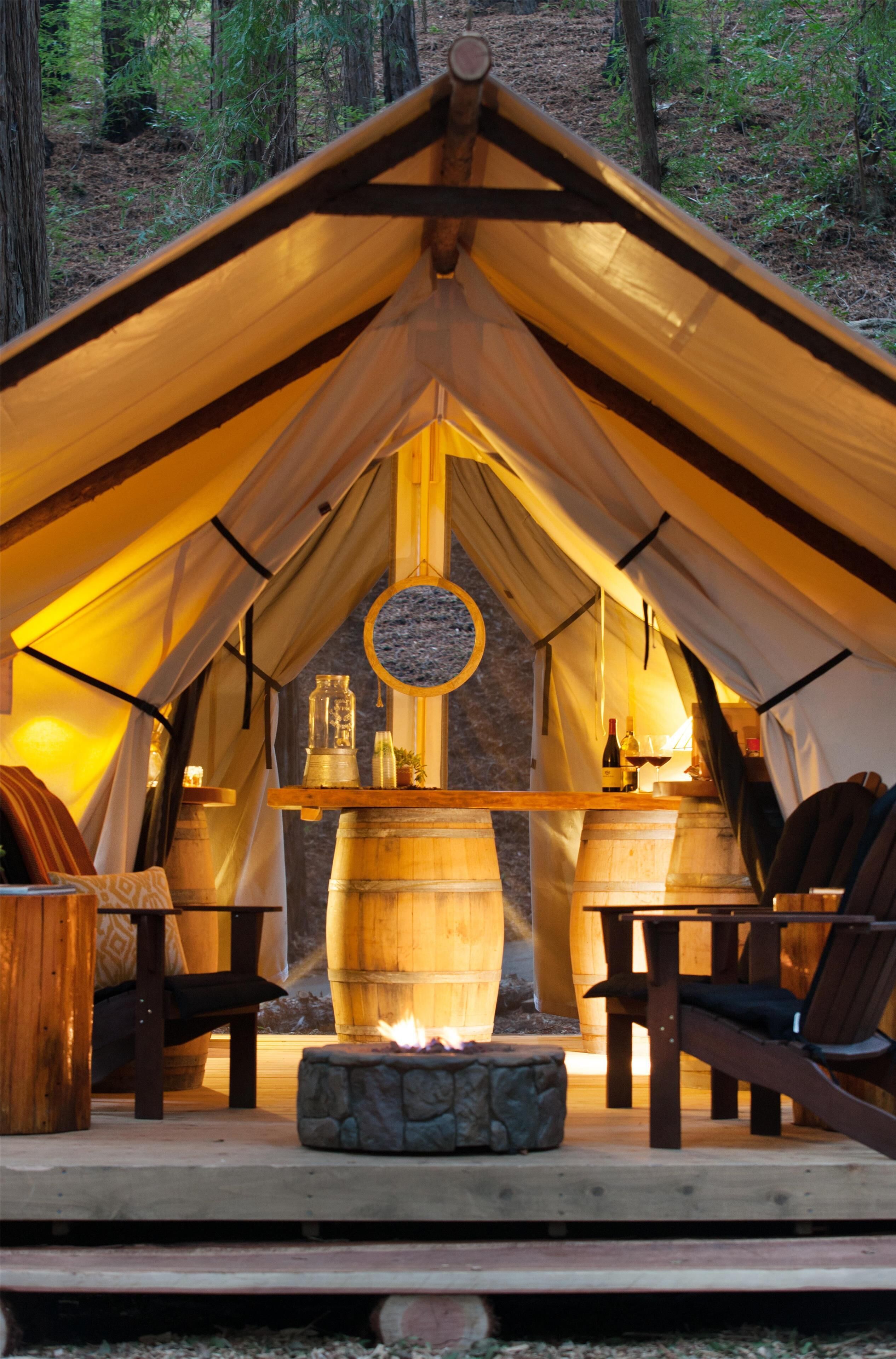 A tent with a stone fire pit, wooden furniture, and a hanging lantern.