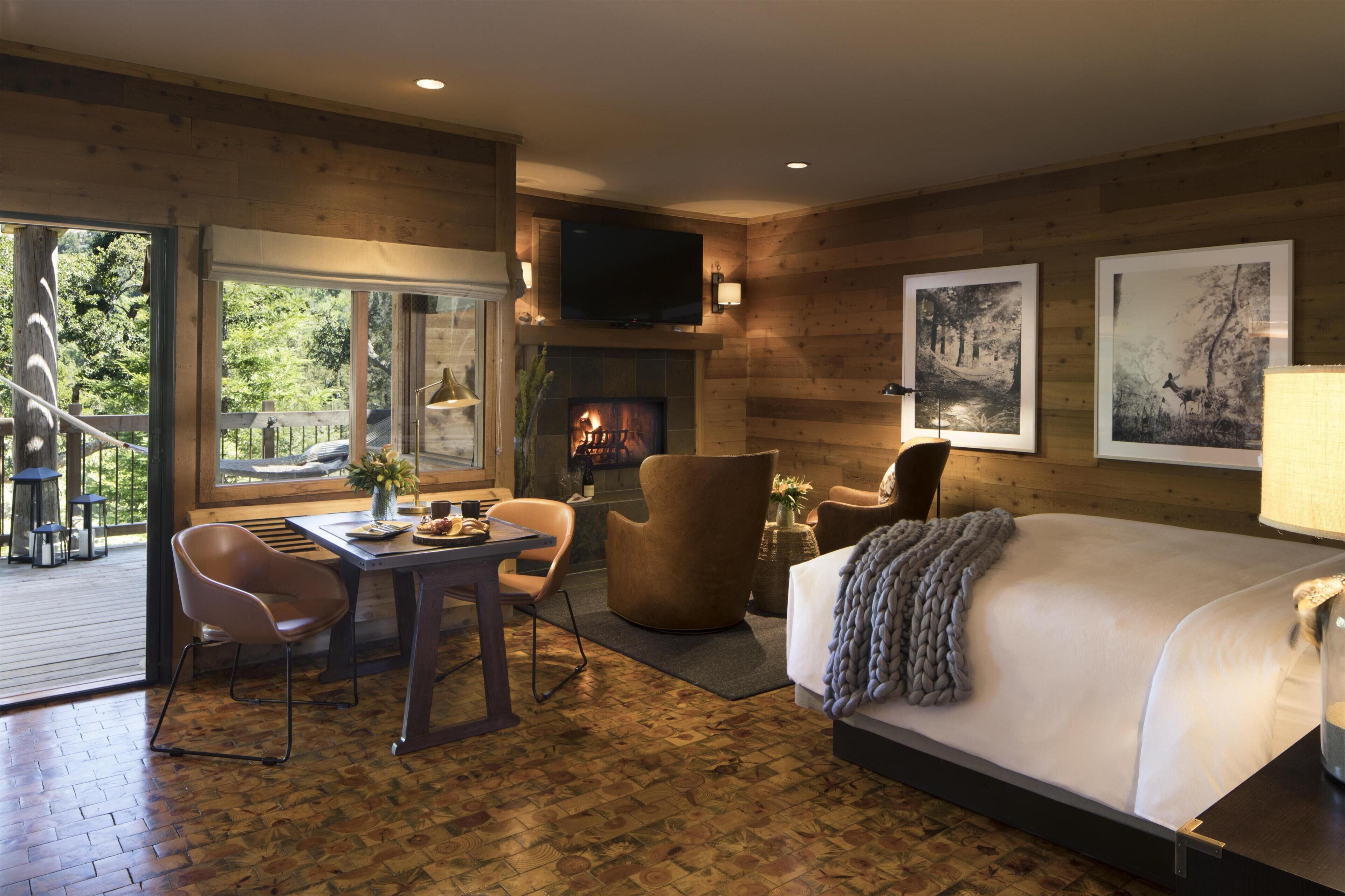 Una habitación con chimenea, televisor montado encima, cama, mesa de comedor con sillas y un ventanal grande.