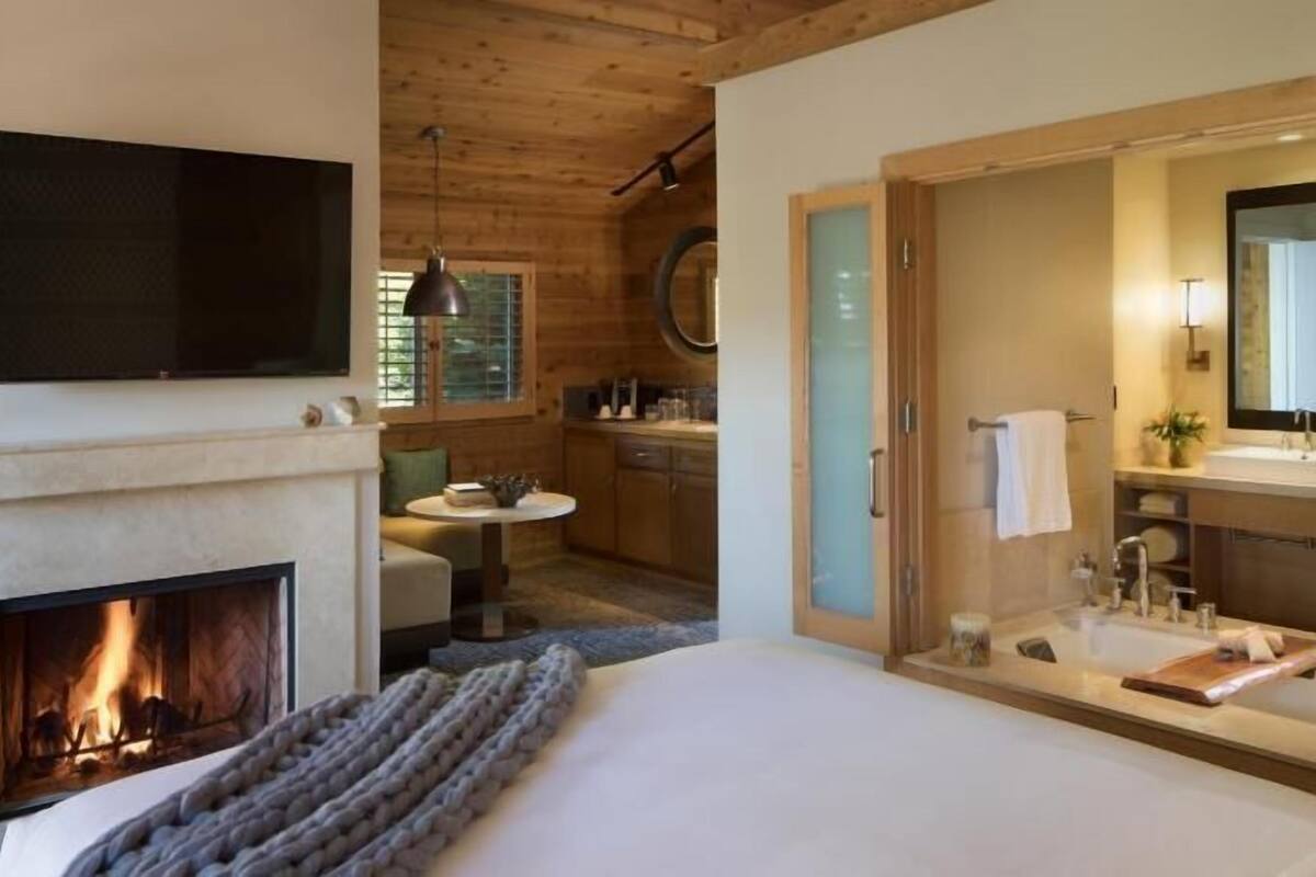 Un dormitorio con chimenea, televisor, zona de comedor y baño con espejo y lavabo.