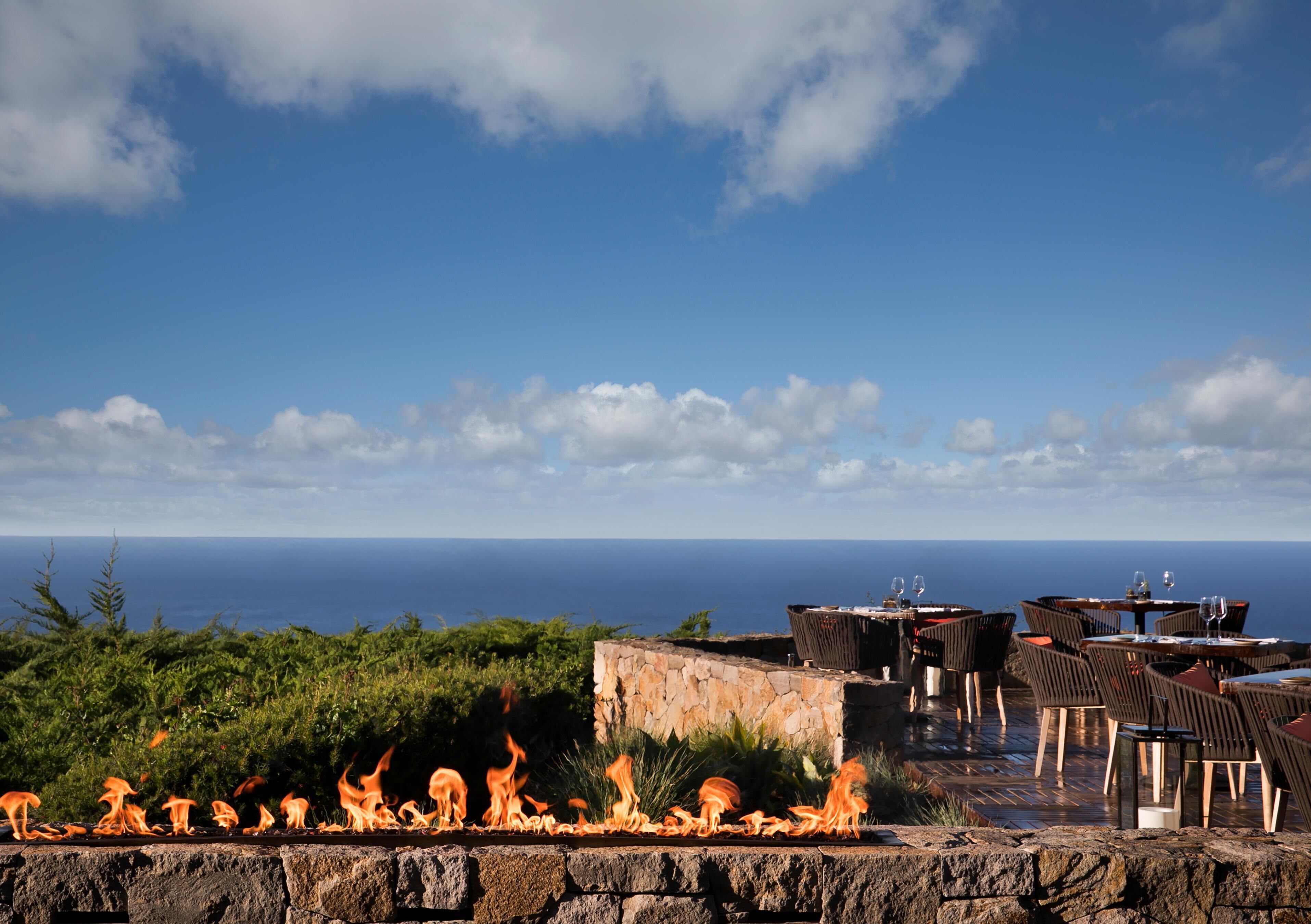 A rooftop terrace with a view of the ocean, outdoor seating, and a fire feature.