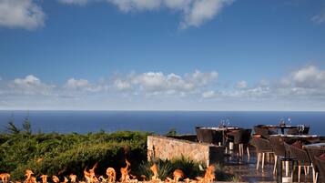 A rooftop terrace with a view of the ocean, outdoor seating, and a fire feature.
