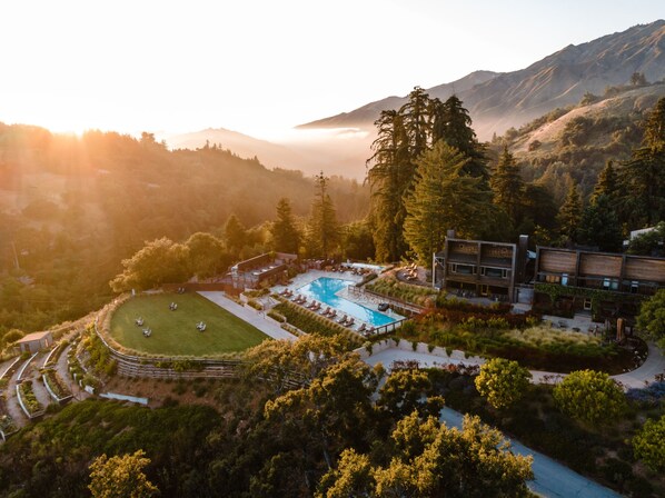 A resort with a swimming pool surrounded by lush greenery and mountains in the background.