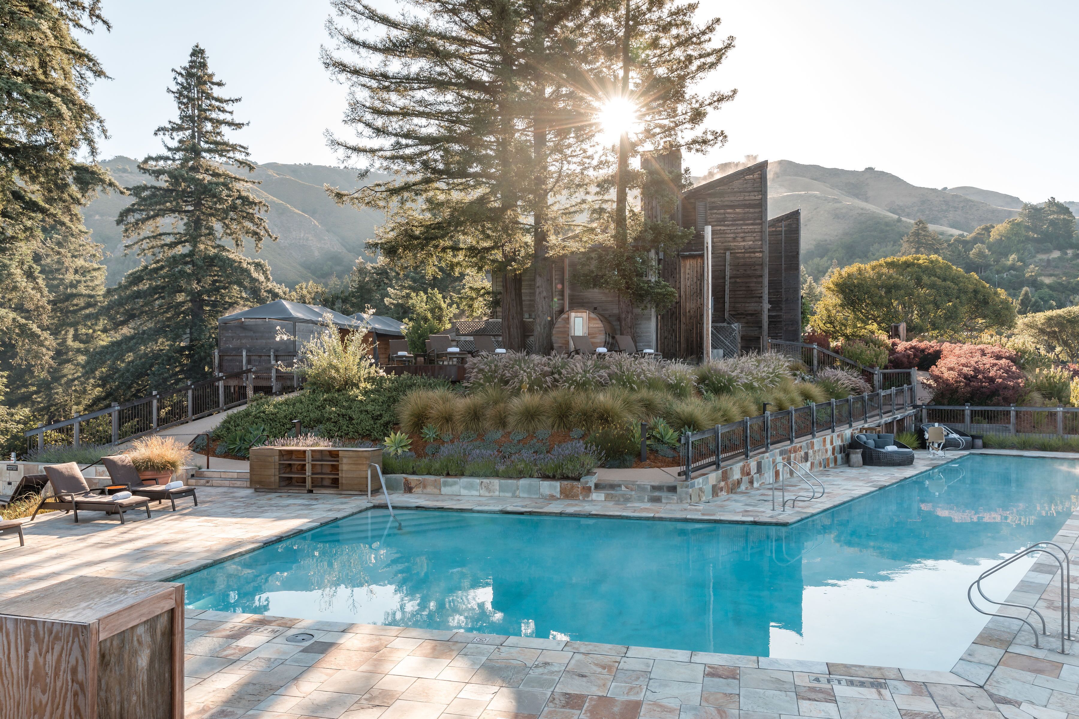 A pool area with a wooden deck, lounge chairs, and a view of mountains.