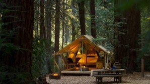 A forested campsite with a yellow tent, a fire pit, and a picnic table. - Alila Ventana Big Sur (Big Sur)