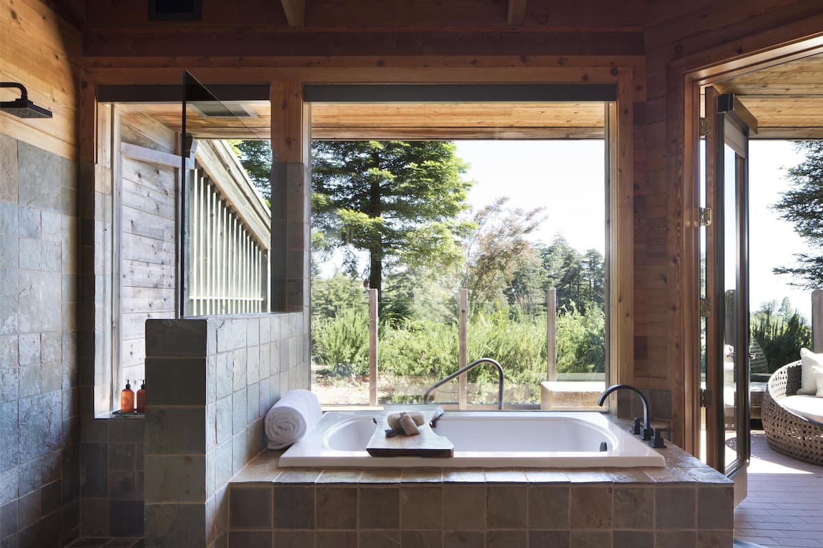 Un baño con una bañera de piedra, una ventana y vistas a árboles.