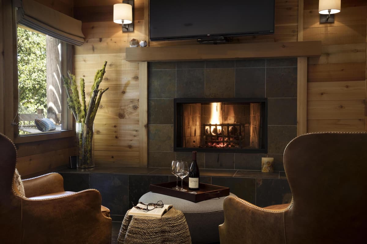 Una habitación acogedora con chimenea, sillones de cuero, televisión y ventana con vista a árboles.